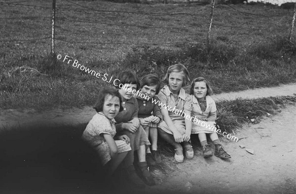 GROUP OF CHILDREN SITTING AT ROADSIDE